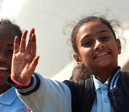 Children in blue school uniforms wave towards the camera.