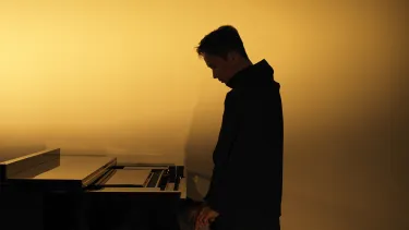 Man standing up and playing piano against a yellow graident background