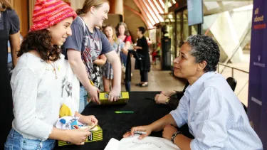A young girl talks to an older woman who smiles back at a book signing desk.