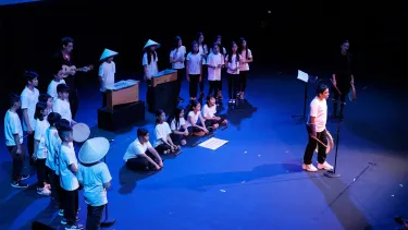 A group of school children in white t-shirts, performing on the stage.