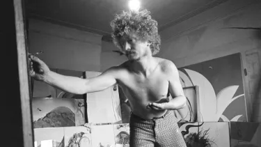 Brett Whiteley paints with a series of unfinished paintings in the background in black and white.