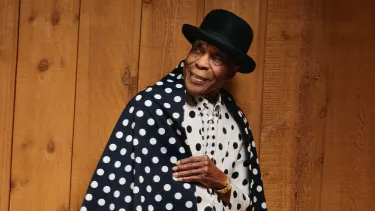 A 90-year-old African American man wears a bowler hat and black and white spotty outfit.
