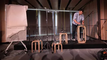The artist sets up glasses of water and clarinets on chairs attached to piping.