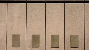 A wall with four plaques on it, with part of the Sydney Opera House in the background.