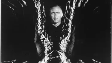 A person standing and looking straight ahead with distorted hands in a pattern around them.