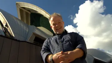 A man in blue shirt in front of Sydney opera house.