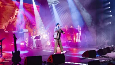 A musician on stage in a suit leads a band.