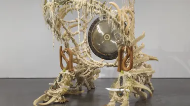 A large cream sculpture with a gong in the centre representing the artists battle with cancer in an exhibit.