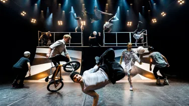 A group of men performing tricks in front of a skate ramp.