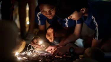 Two young boys crouched over a project featuring bright lights.