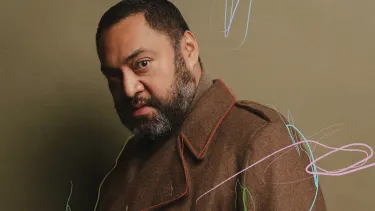 A man wearing a brown wool coat looking sidelong against a olive green background with subtle scribbled marks in pink, red, light blue and green.