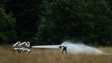 Three people dressed in silver suits blast water at a person with a powerful hose.
