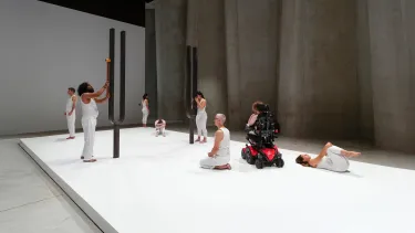 Performers standing and sitting around two large sculptural tuning forks.