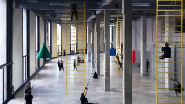 People interact with a series of ropes and ladders suspended from the ceiling in an art gallery.