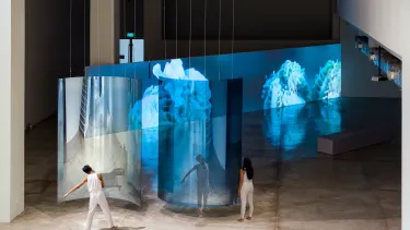 Performers standing in front of large blue translucent screens in an art gallery.