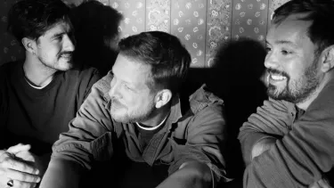 Three white men sit casually smiling in black and white.