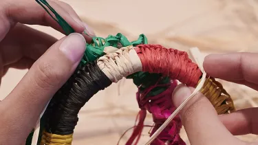 A close up of hands weaving using a traditional Aboriginal technique