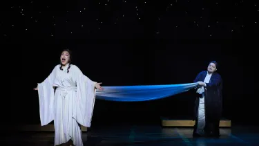 A woman in white sings as a man in blue pulls her clothing towards him.