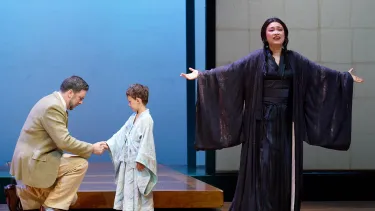 A woman sings with arms outstretched as a boy behind her shakes the hand of a kneeling man.