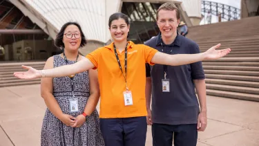 Three opera house staff from different departments stand smiling on the Opera House steps.