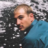 Headshot of Solly Frank wearing a blue collared shirt, looking over one shoulder, with a body of water in the background.
