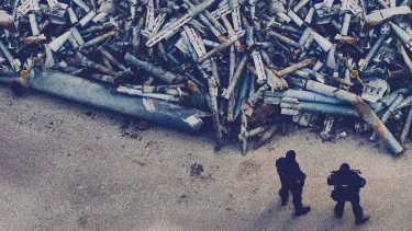 Two soldiers stand in front of a pile of discarded missiles.