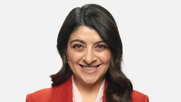 A smiling woman with dark brown hair, wearing a red blazer against a light grey background.