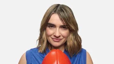 A woman with light brown shoulder length hair wearing a blue sleeveless jersey and holding a red football.