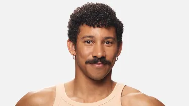 A headshot of a man with curly dark hair, wearing a peach coloured singlet against a light grey background.