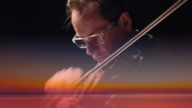 A violinist plays in front of a superimposed sunset