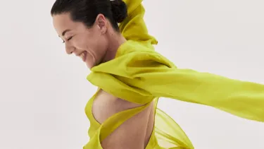 A dancer in bright yellow, in motion against a light grey background.