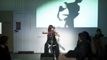 A female cellist plays in front of a projected image of a silhouette dancing.