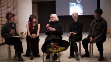 A panel discussion between artists in front of a bouquet of flowers.