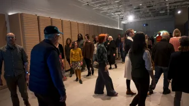 Artists and participants walk around the room towards a projected image on the wall.