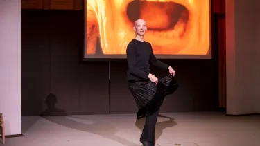 An artist stands on one leg in front of a projected image of an open mouth.