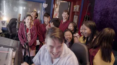A man surrounded by school kids in a recording studio.